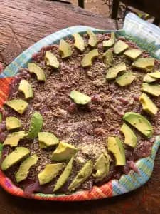 A colorful platter of raw meat topped with sliced avocado and sprinkled with cheese.