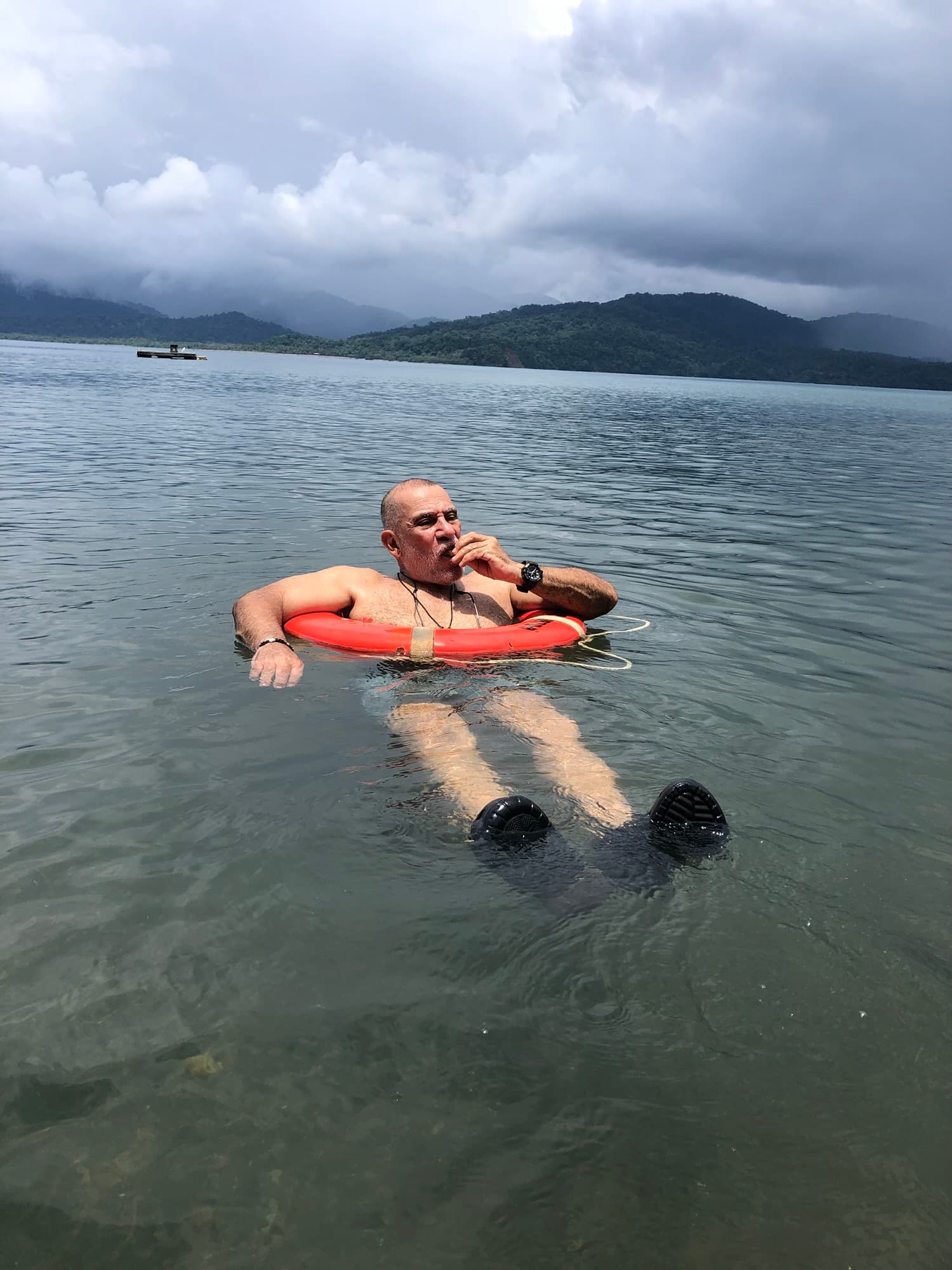 A man relaxes in a lifebuoy while floating in calm water under a cloudy sky.