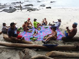 A group of people enjoying a picnic on a beach with a colorful blanket.
