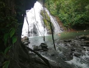 A waterfall cascades into a turquoise pool surrounded by lush greenery and visitors.