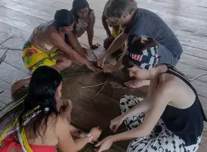 A group of people collaboratively weaving materials on a wooden floor.