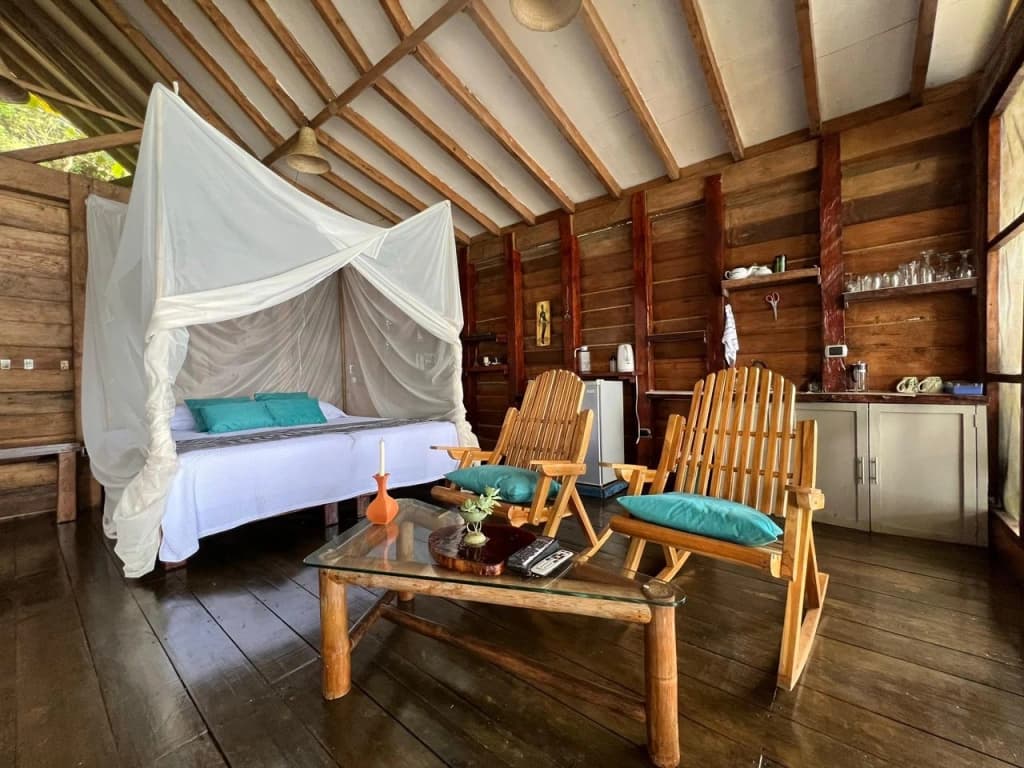 A cozy wooden bedroom with a canopy bed, two chairs, and a kitchenette.