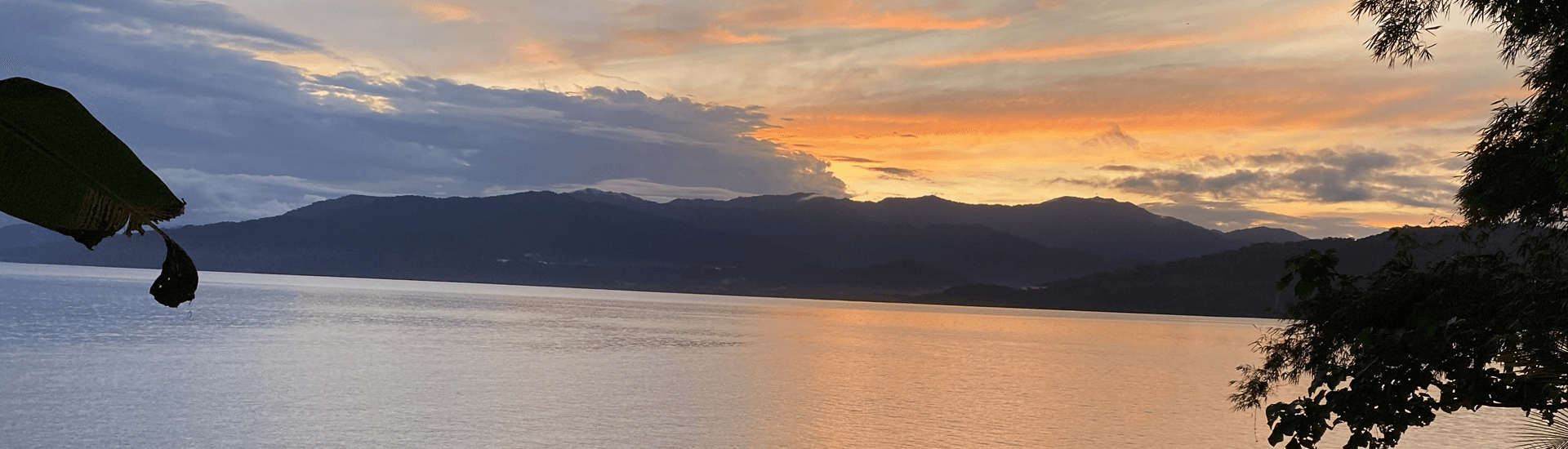 A serene sunset over calm waters with mountains in the background.