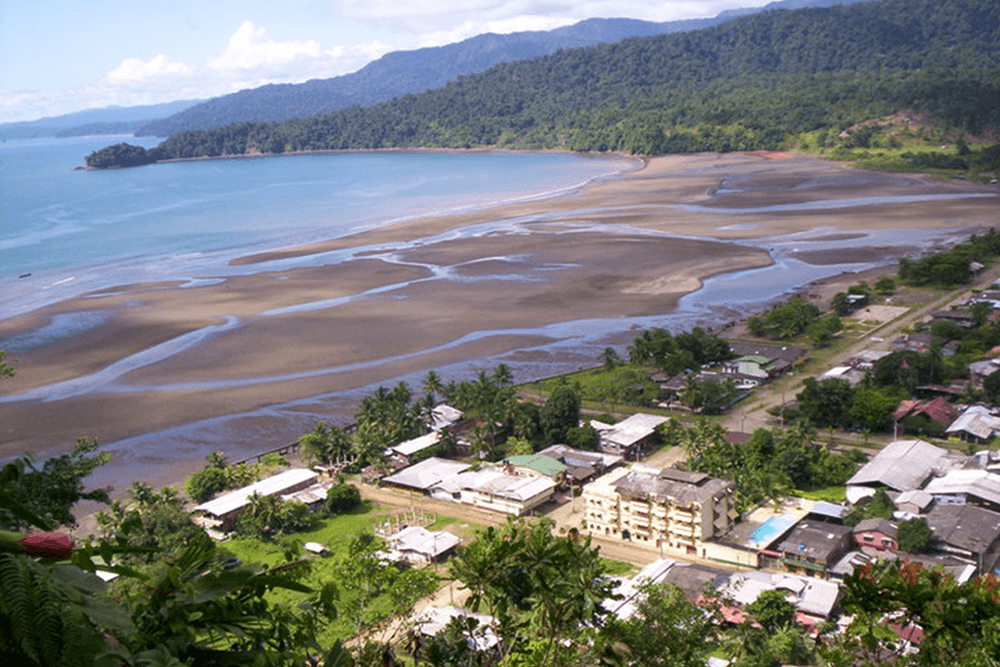 Aerial view of a coastal town with sandy shores and green hills in the background.